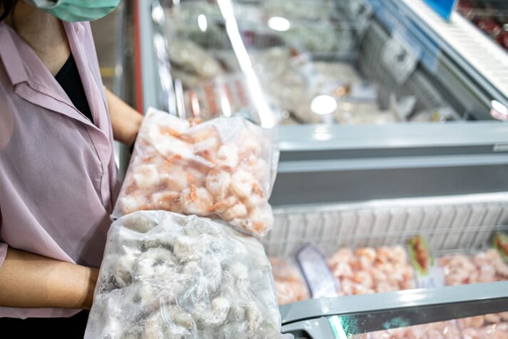 Person holding frozen shrimp above a grocery case
