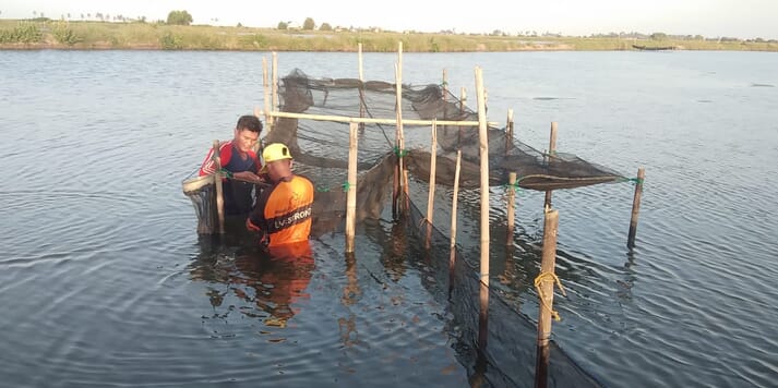 Two people standing near fish nets in the water