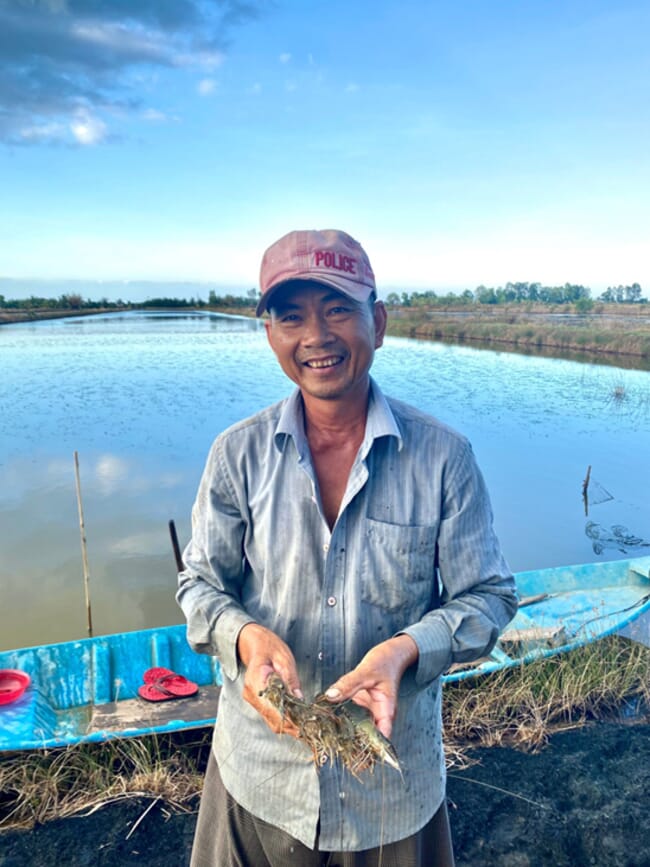 A man holding some shrimp, beside a pond.