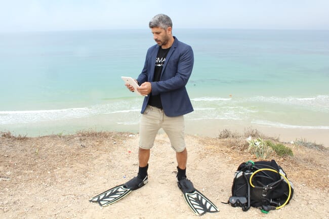 A CEO wearing a suit and diving fins accessing aquaculture farm data from his phone.