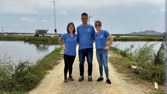 Three people standing together beside shrimp ponds.