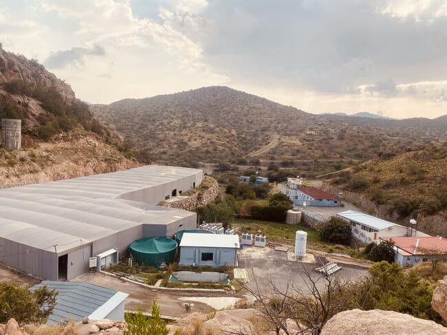 The exterior of an indoor fish farm in an arid, hilly landscape.
