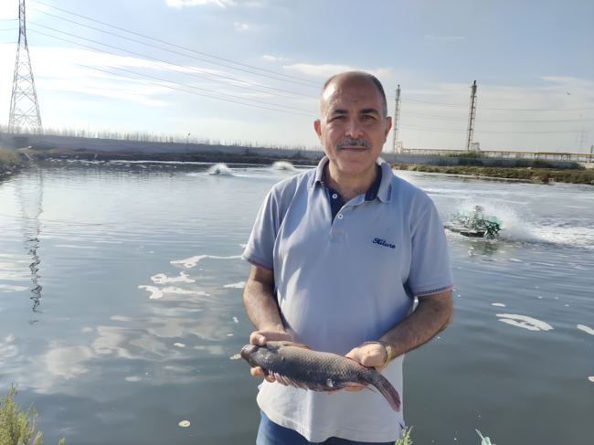 Um homem segurando um peixe em frente a um lago.