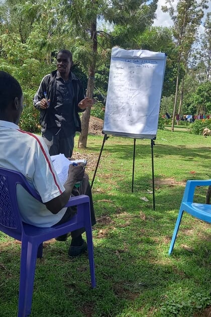 Young man standing outside next to a flip chart talking to a person sitting in a chair