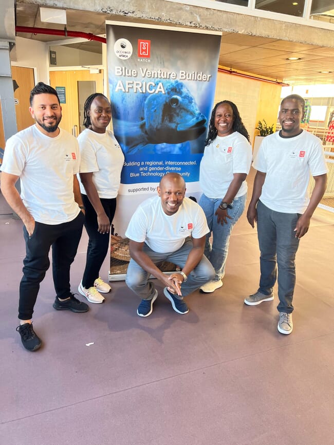 Five people standing beside a sign for a training programme.