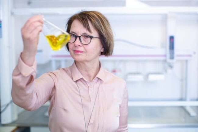 A woman holding up a flask of liquid in a lab.
