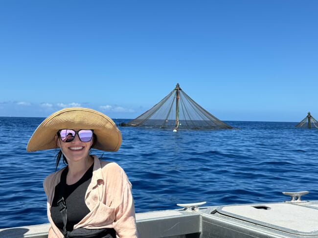 Uma mulher em um barco, em frente a uma fazenda de peixes.