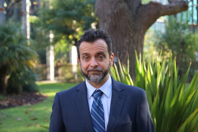 A portrait of a professor in a suit on an Australian university campus.