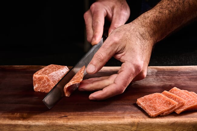 A piece of cell-based tuna being sliced with a knife.