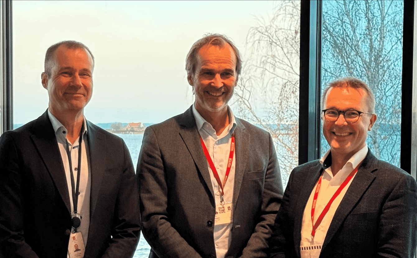 Three men in suits posing for a photo after signing an agreement.