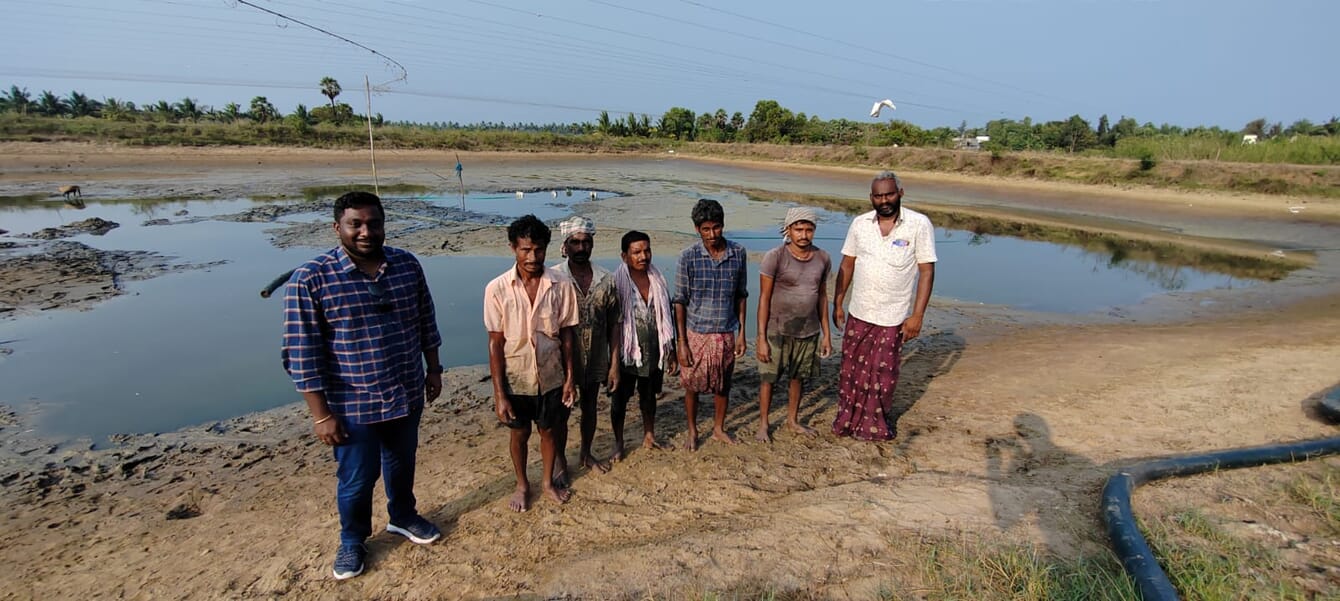 A group of workers in India nearby an empty shrimp pond.