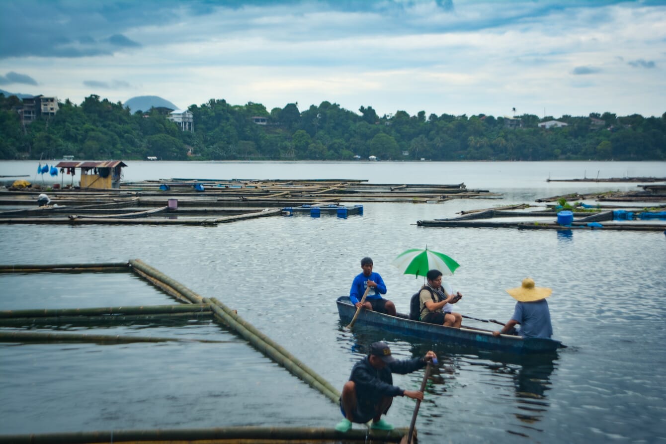 Fish farmers in small boats beside wooden fish pens.