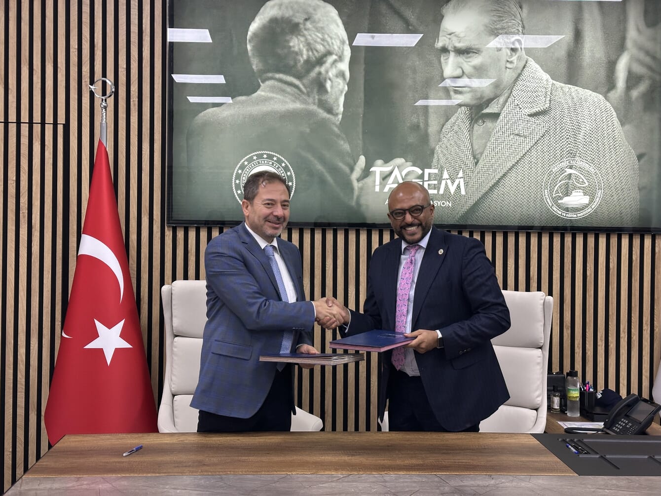 Two representatives shaking hands after an agreement infront of a Turkish flag.