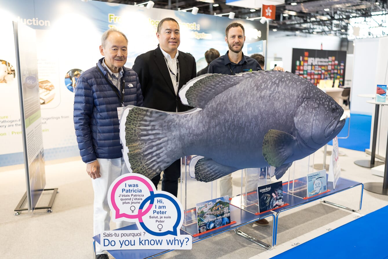 Three men at an exhibition standing infront of a large fish.