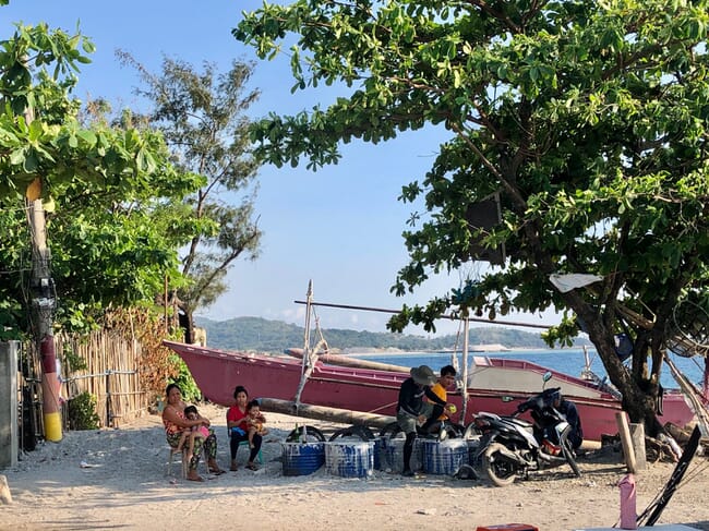 Fisherfolks with families in next to fishing boats and equipment.