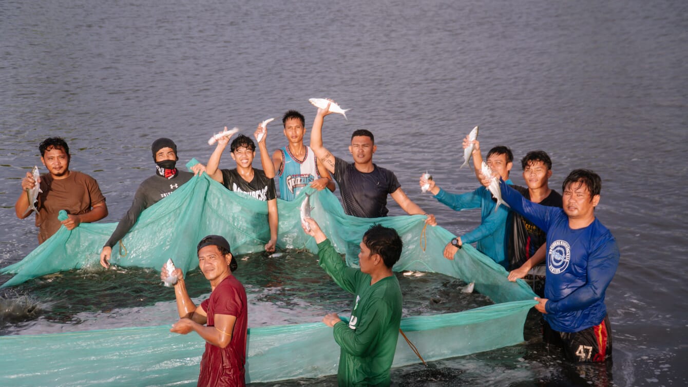 A group of farmers in the water collecting milkfish from their pond in the Philippines.
