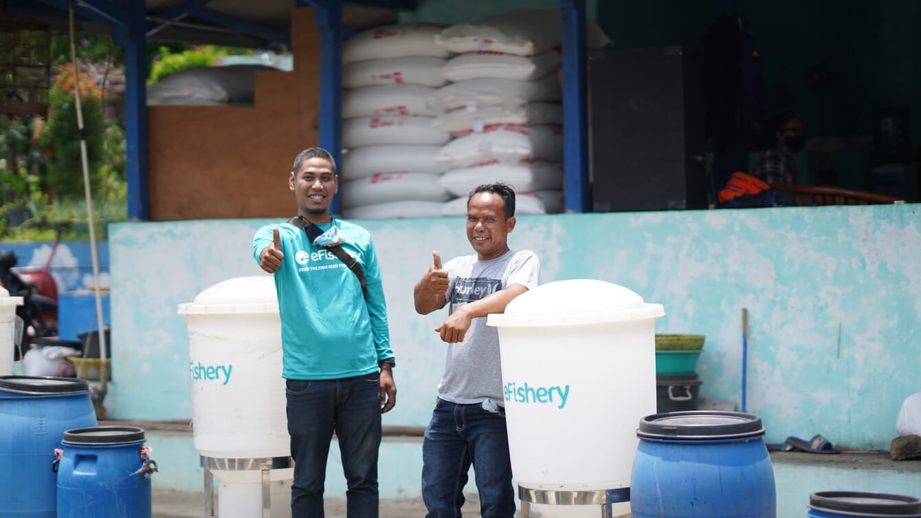 Two men with their thumbs up next to shrimp feeders