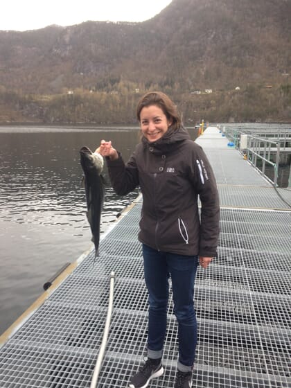 Woman standing on a jetty holding a fish in one hand