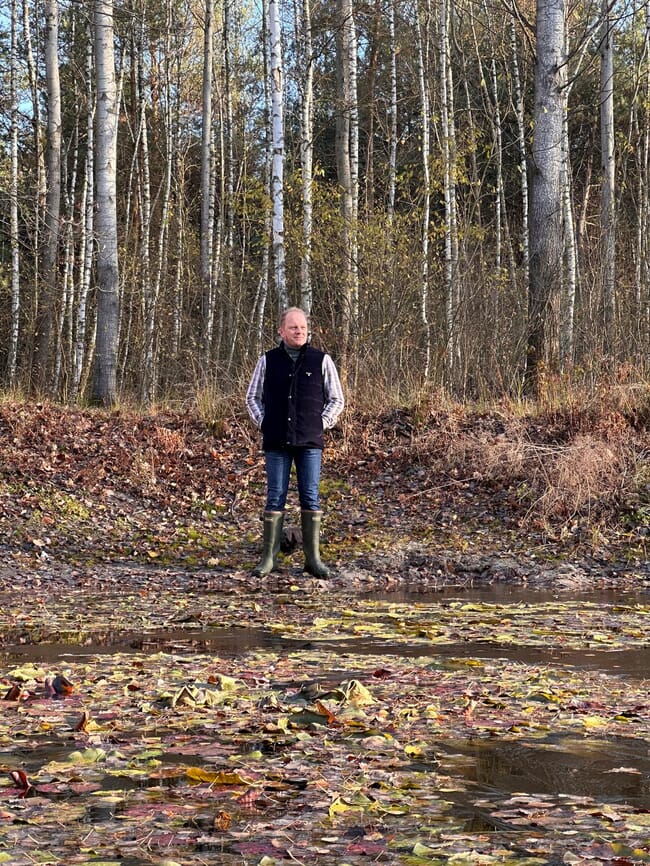 A man standing in front of a wood.