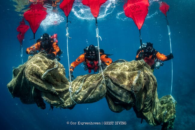 Tres buceadores bajo el agua con un gran trozo de basura marina