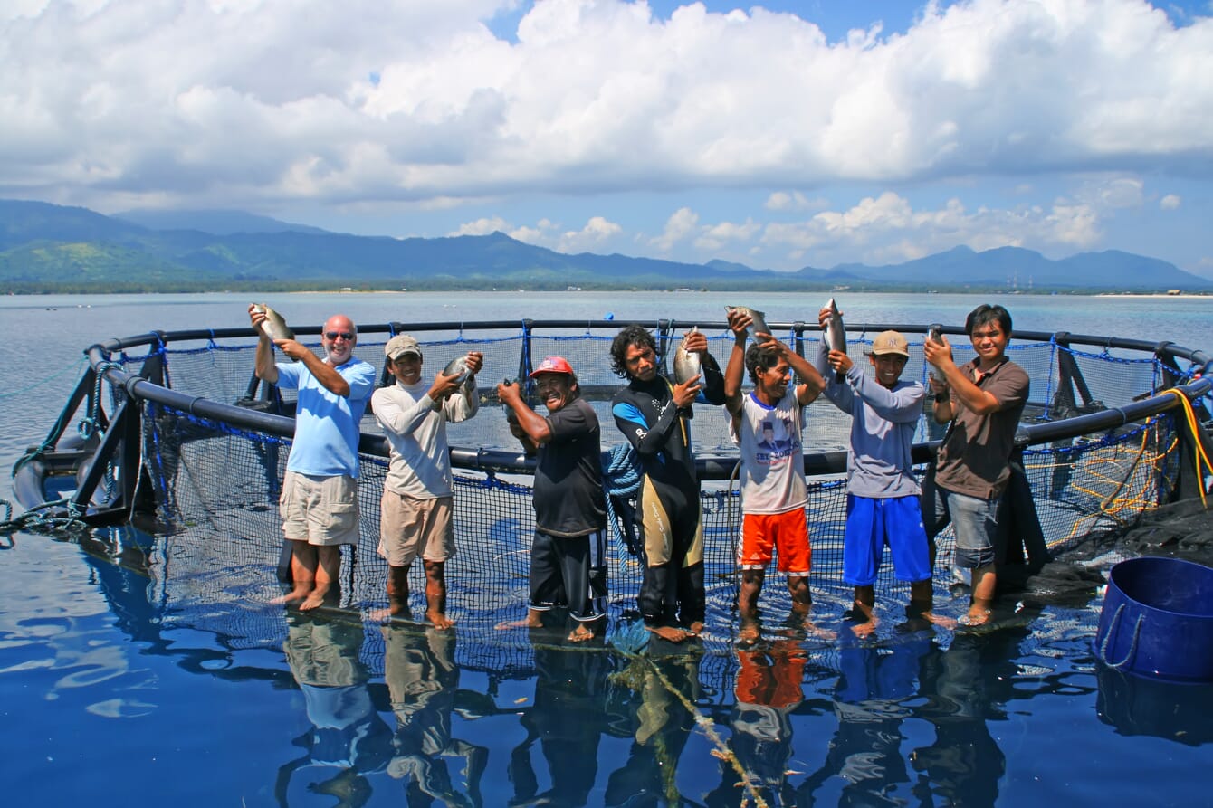 Grupo de pessoas segurando peixes em uma gaiola na água