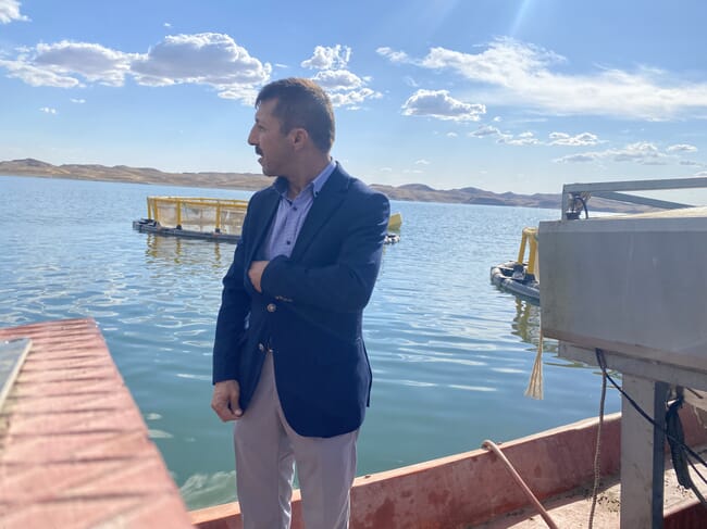 A man in smart clothing standing beside some fish cages.