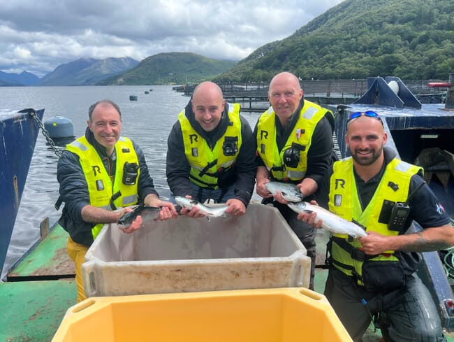 cuatro hombres al borde de un lago, cada uno con un salmón en la mano