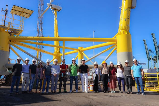 A group photo in front of a large yellow industrial structure.