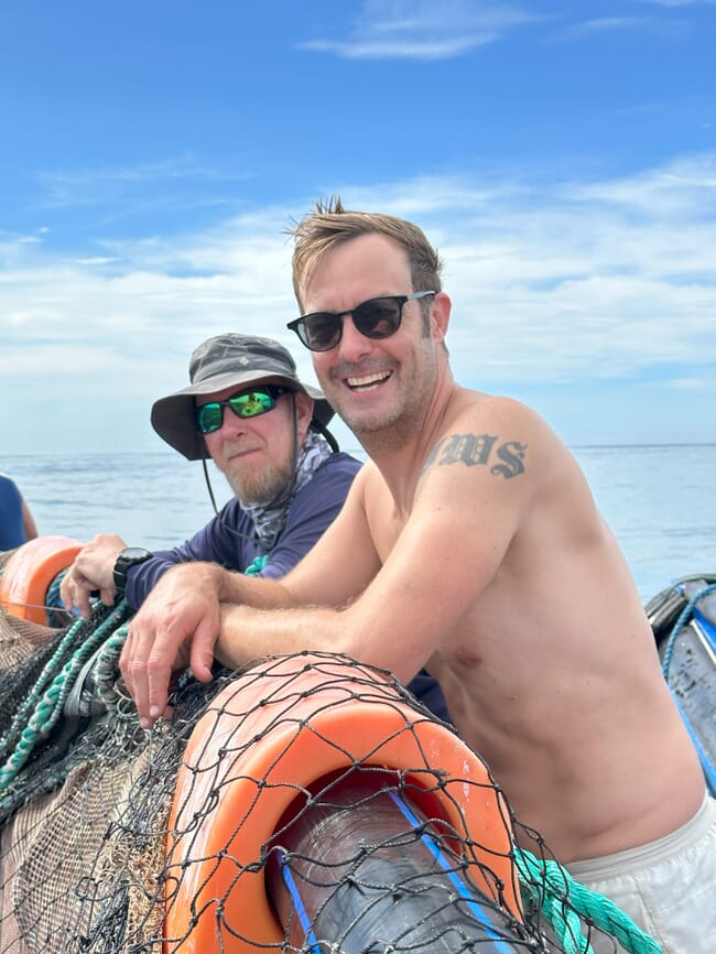 two men leaning on the rail of a fish pen