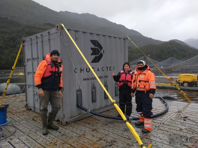 Three people beside a large grey container.