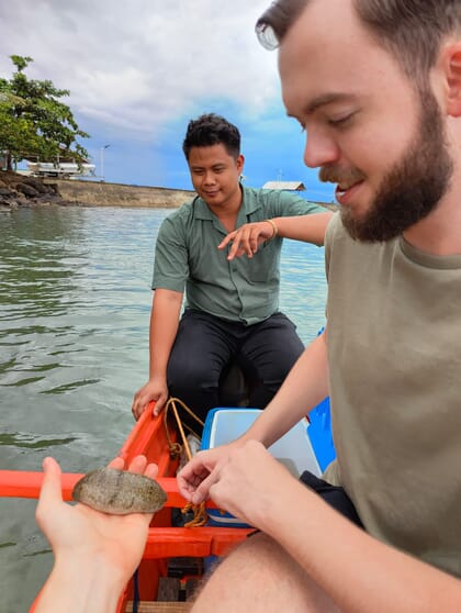 three people in a boat holding a sea cucumber