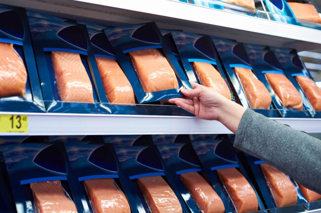 Consumer picking up packet of salmon from supermarket fridge
