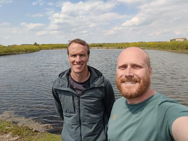 Two men standing beside a pond.