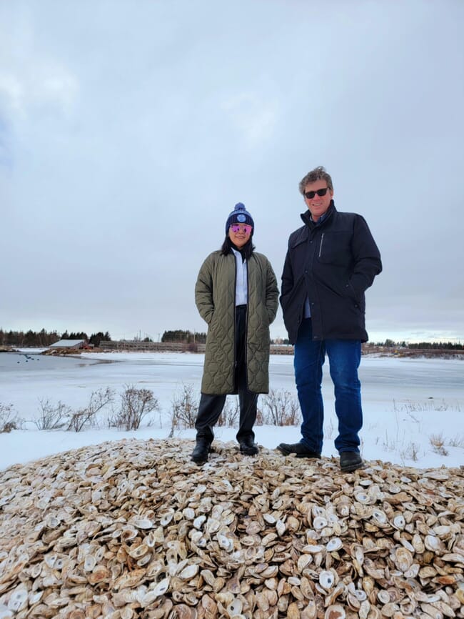 Two people standing on a huge pile of oyster shells.