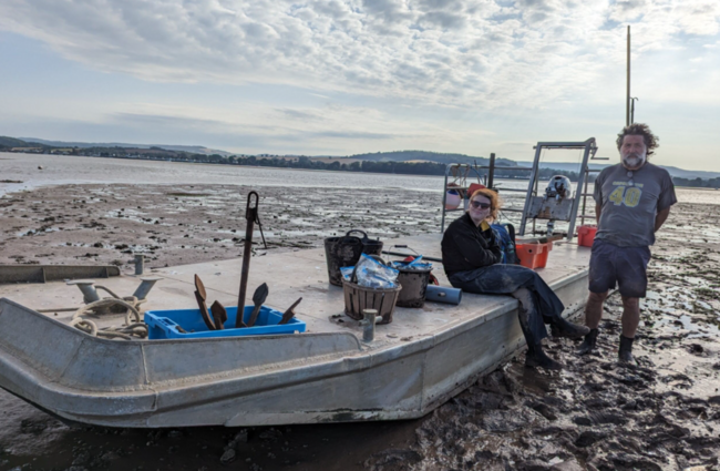 Two people beside a boat on a mudflat.