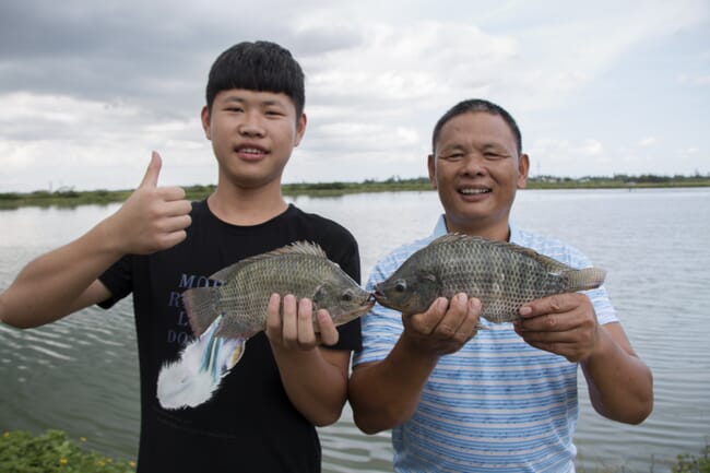 two men holding tilapia