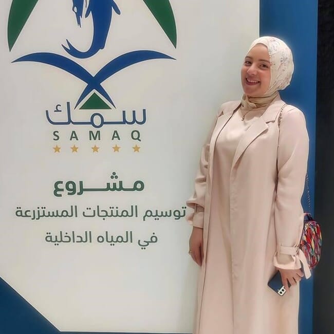Mulher ao lado de placa da Saudi Aquaculture Society (Sociedade Saudita de Aquicultura)