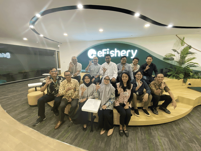 A group of eFishery's employees sit in front of an eFishery's sign.